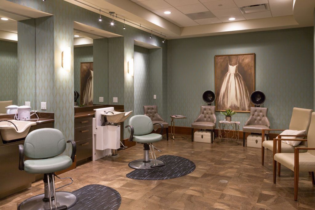 A cozy and neatly arranged salon interior with chairs, mirrors, hairdryers, and artwork on the wall.