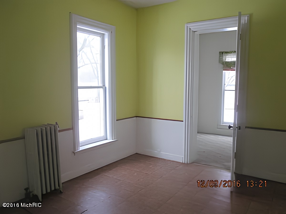 An empty room with yellow walls, featuring a window, doorway, and radiator.