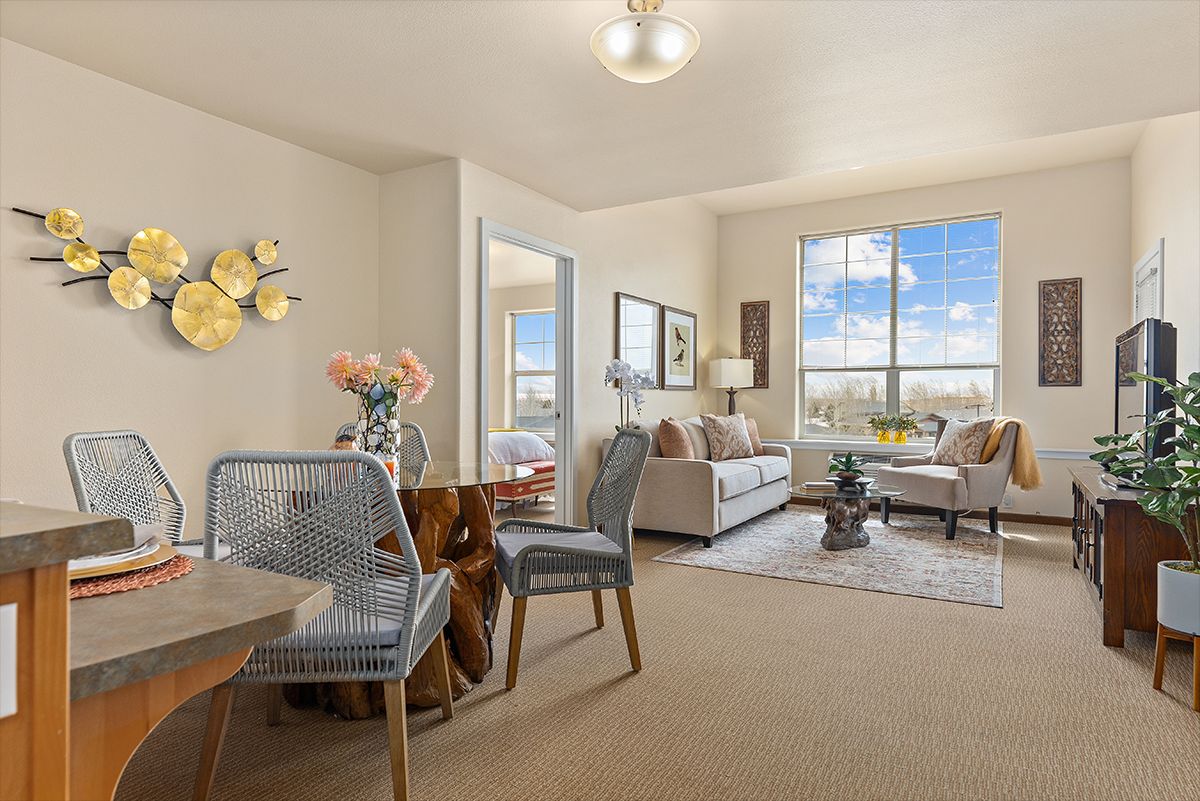A bright and cozy living room with a dining area, featuring modern furniture and a large window offering a scenic view.