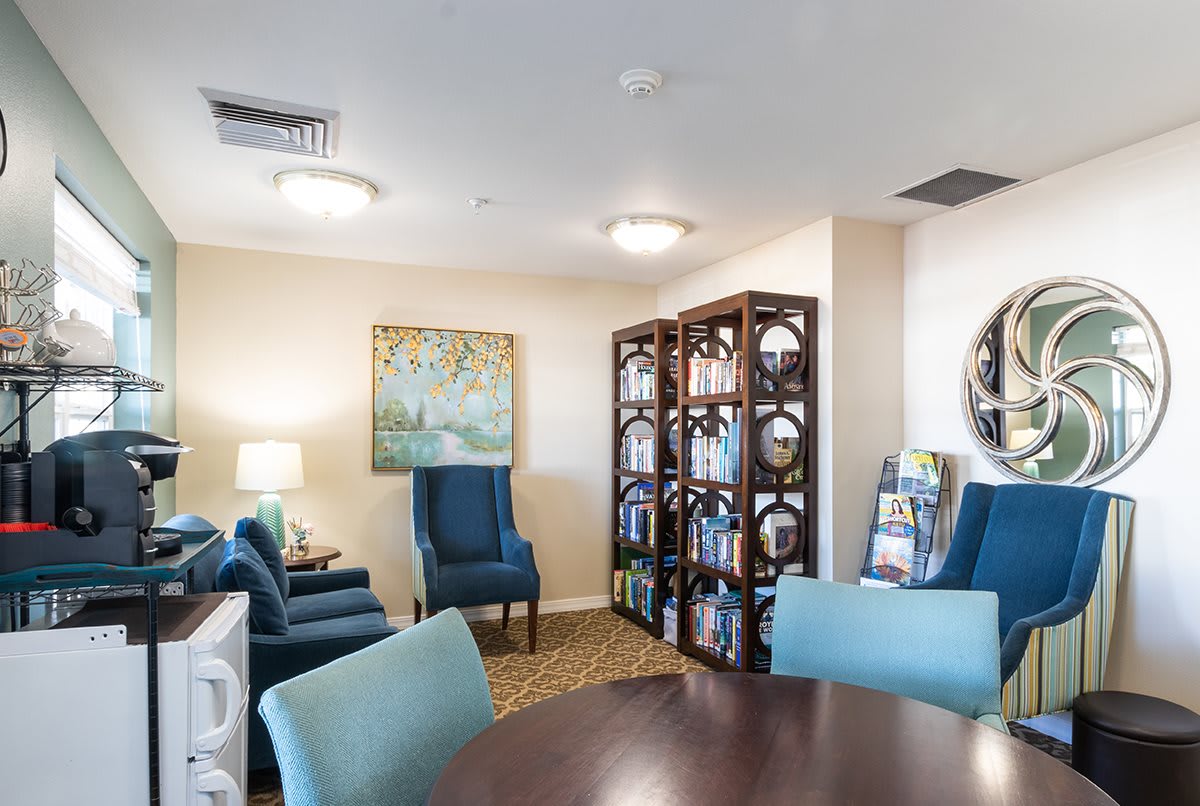 A cozy lounge area featuring comfortable chairs, a round table, bookshelves filled with books, and decorative artwork on the walls.