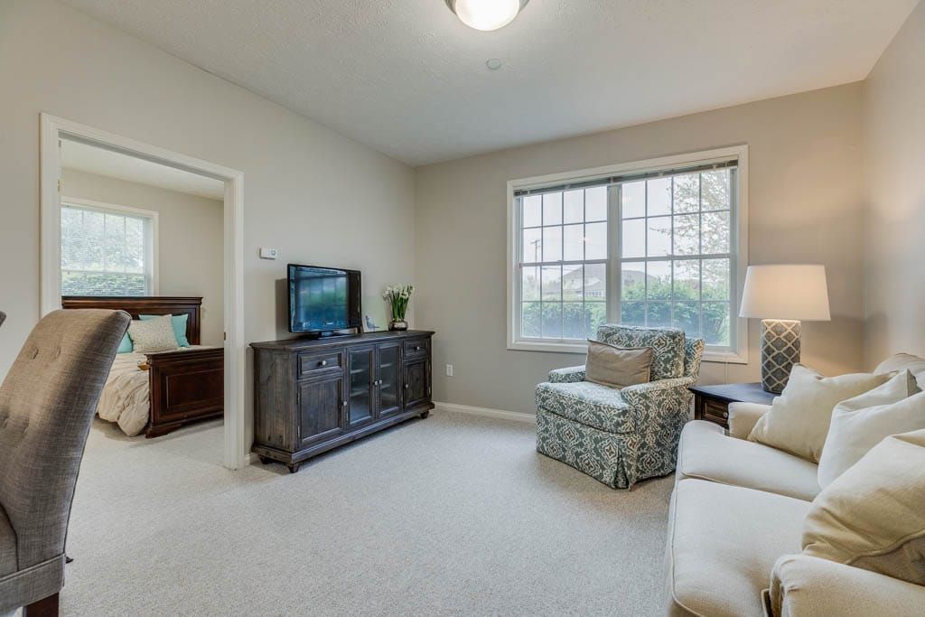 A cozy living room with a TV, comfortable seating, and ample natural light from a large window.