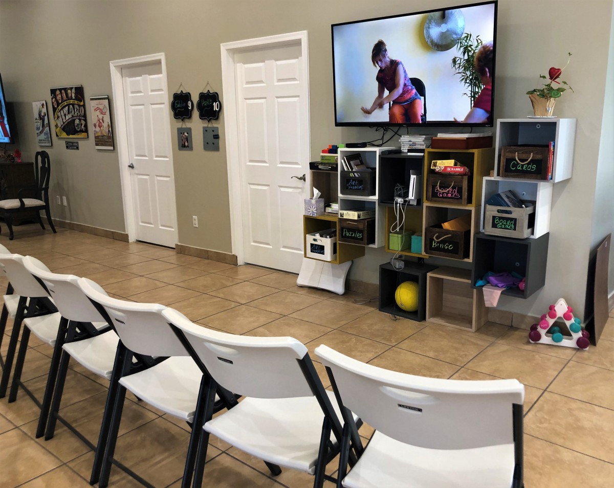 A waiting room with white chairs, a television on the wall, and toys on shelves.