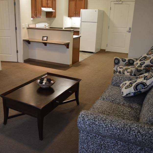 A cozy apartment living area with a sofa and coffee table, adjacent to a kitchen.