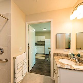 A bathroom with a granite countertop and a view into the kitchen area.