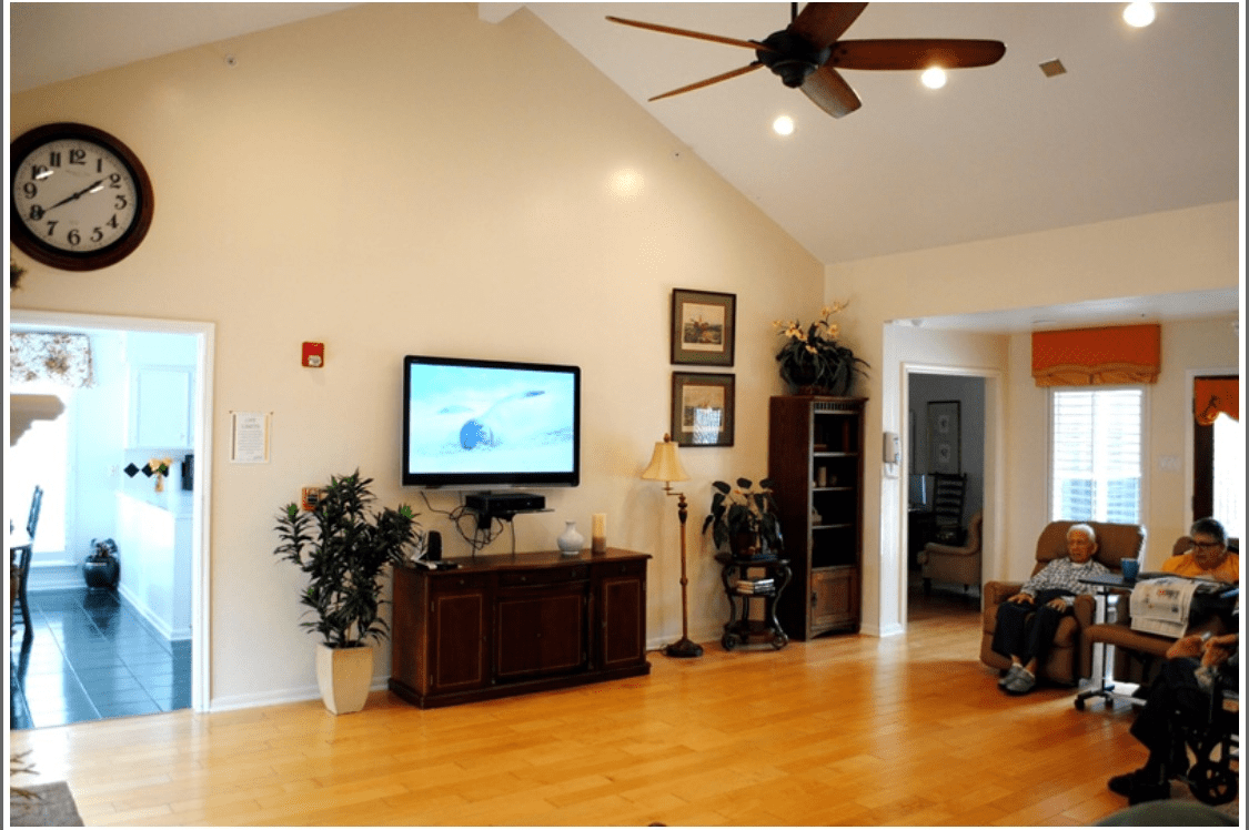 A cozy living room with a wall-mounted television, wooden flooring, and a ceiling fan.