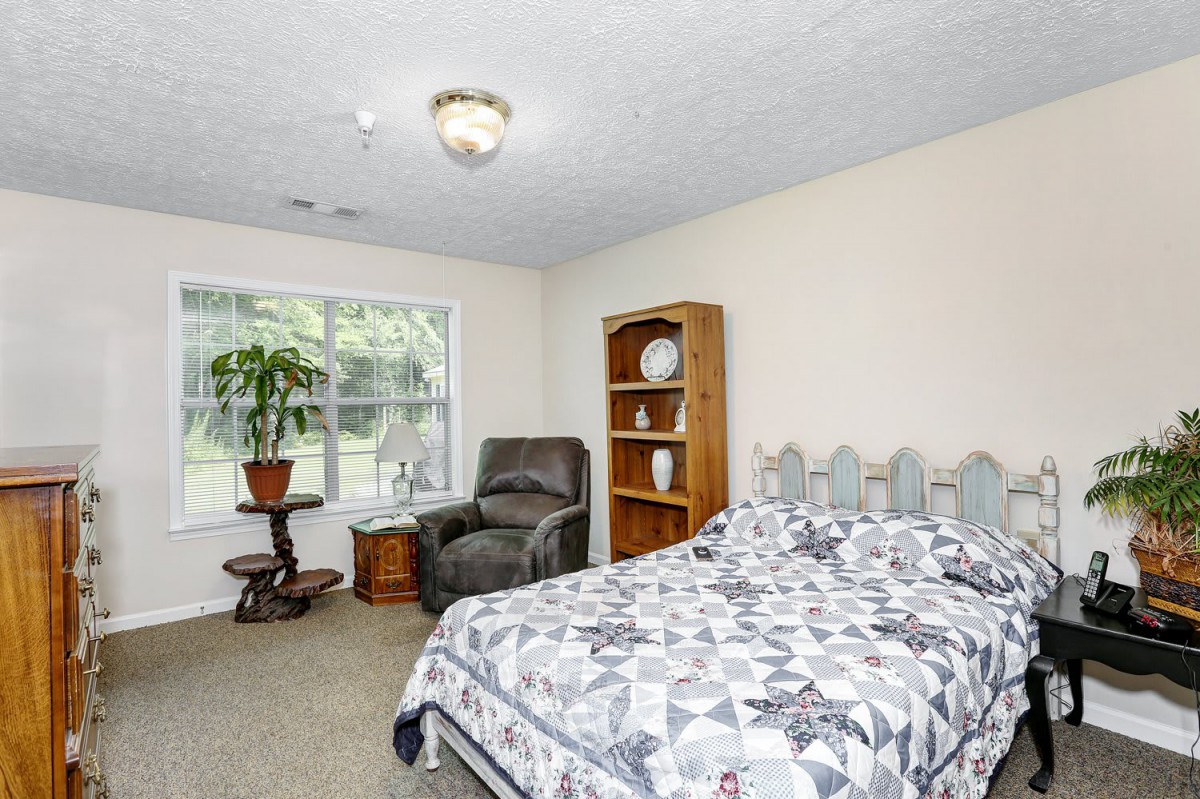 A cozy bedroom with a bed, armchair, and bookshelf near a large window.
