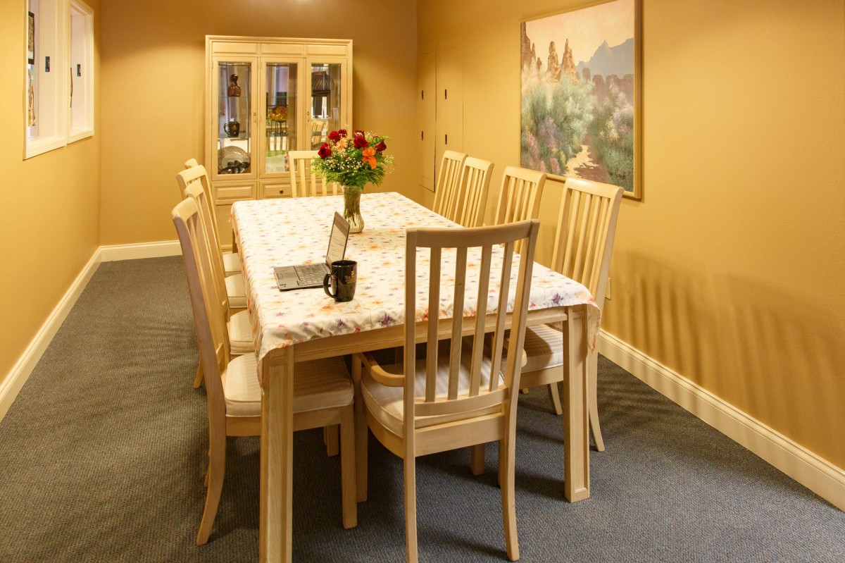 A cozy dining room featuring a wooden table set with chairs and a vase of flowers.