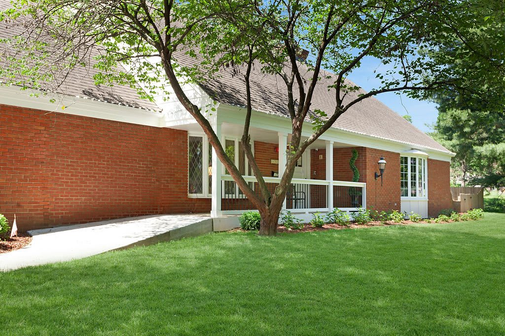 A brick house with a well-maintained lawn and a large tree in the front yard.