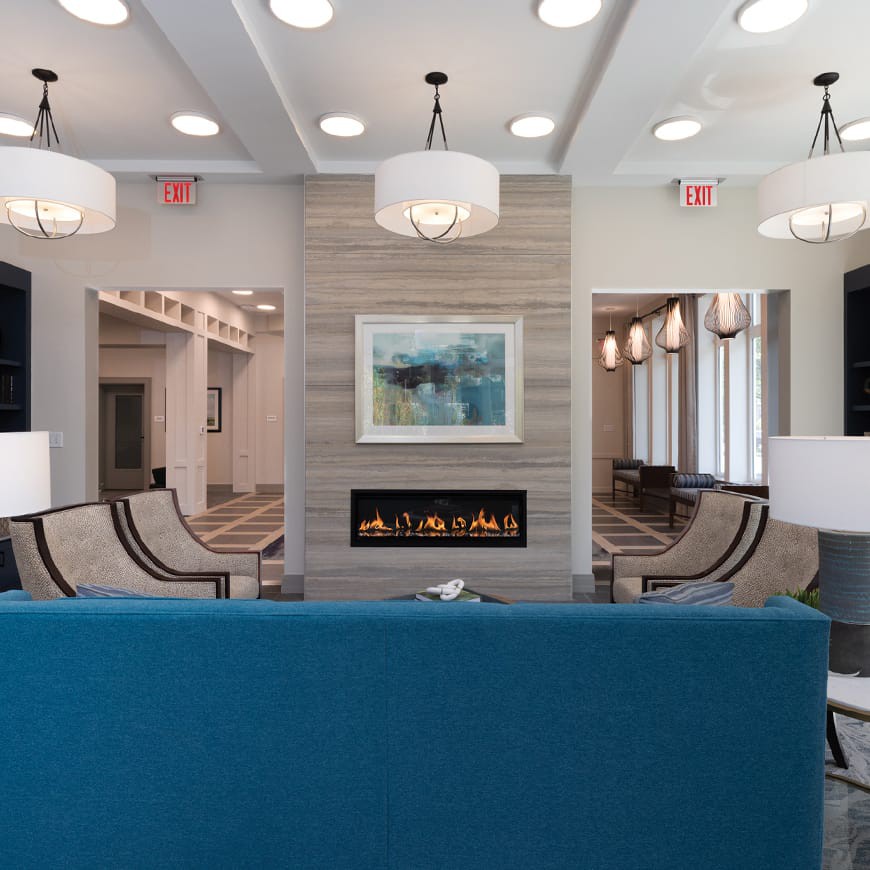 A modern living room with a blue sofa, centered around a sleek fireplace and elegant lighting fixtures.