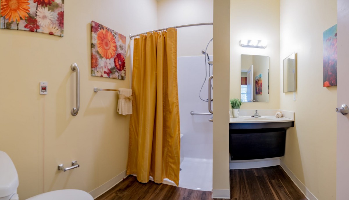 A well-decorated bathroom featuring a shower with a yellow curtain, a sink with a mirror above, and floral artwork on the wall.
