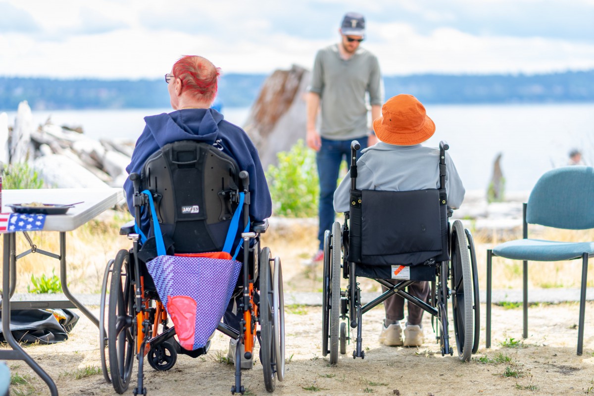 Two people in wheelchairs enjoying a day by the lake with a friend.