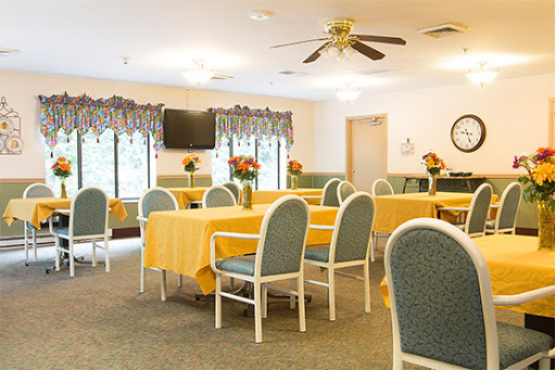 A bright and inviting dining area, furnished with tables covered in yellow tablecloths and comfortable seating, ideal for community gatherings.
