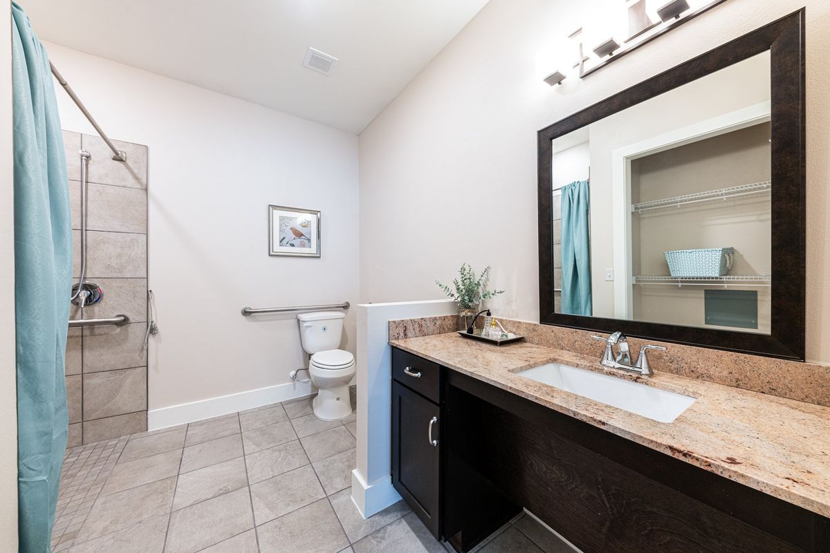 A modern, spacious bathroom with a large mirror and sink area, featuring a tiled floor and a toilet in the corner.