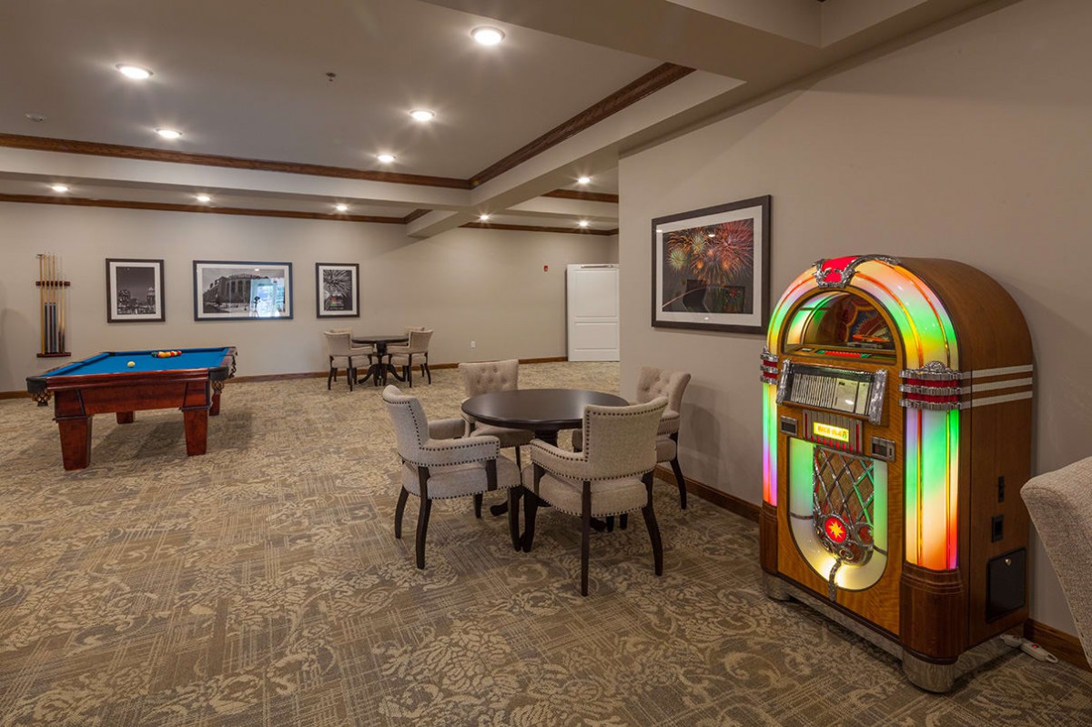 A cozy recreational room featuring a jukebox, pool table, and seating area with warm lighting.