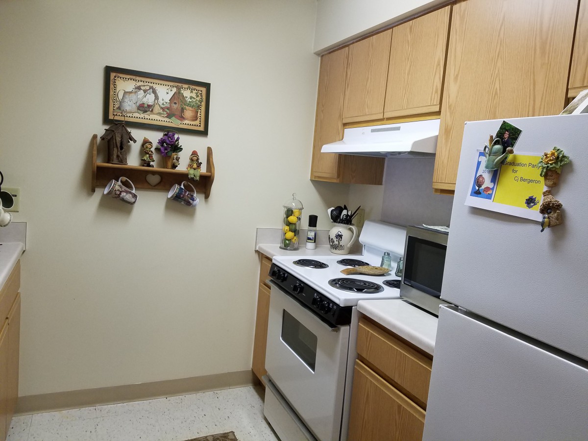 A cozy kitchen with traditional wooden cabinets, a stove, refrigerator, microwave, and decorative wall art.