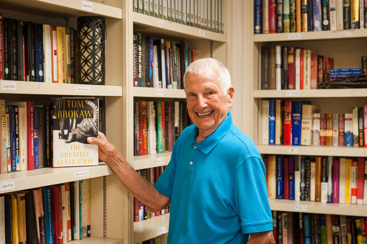 A man smiling while standing in front of a bookshelf filled with books.