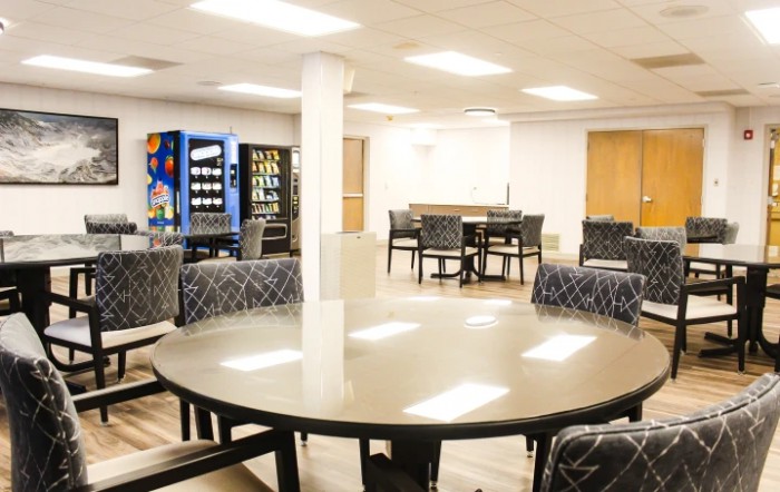 A spacious break room featuring round tables, chairs, and vending machines.