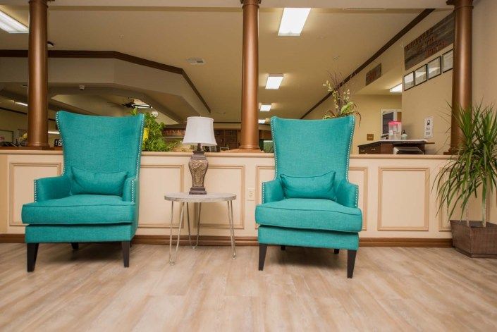 Two teal chairs in a cozy lobby setting with a small table and lamp.