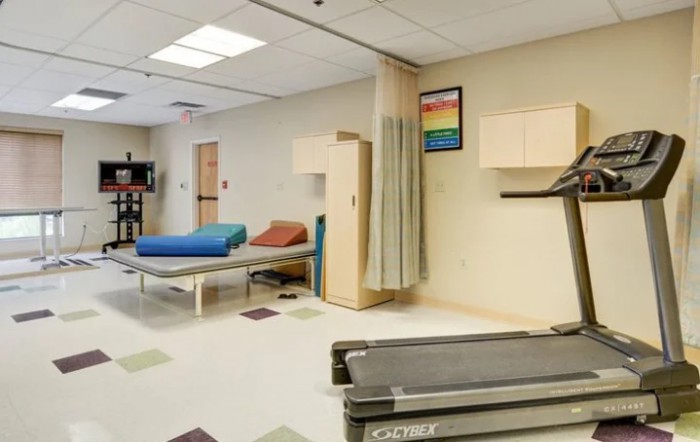 A physical therapy room equipped with a treadmill, therapy beds, and medical furnishings.