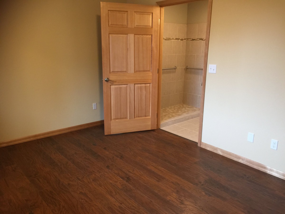 An empty room with wooden flooring and an open closet door showing shelves.