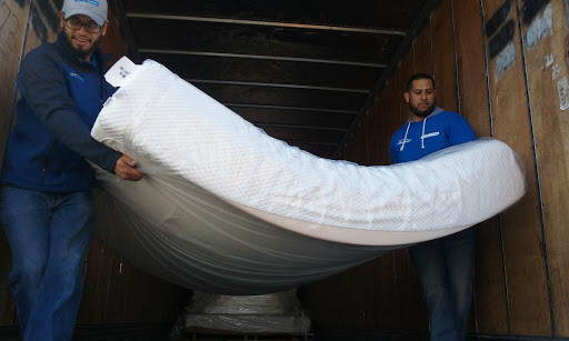 Two individuals loading a mattress into a truck.
