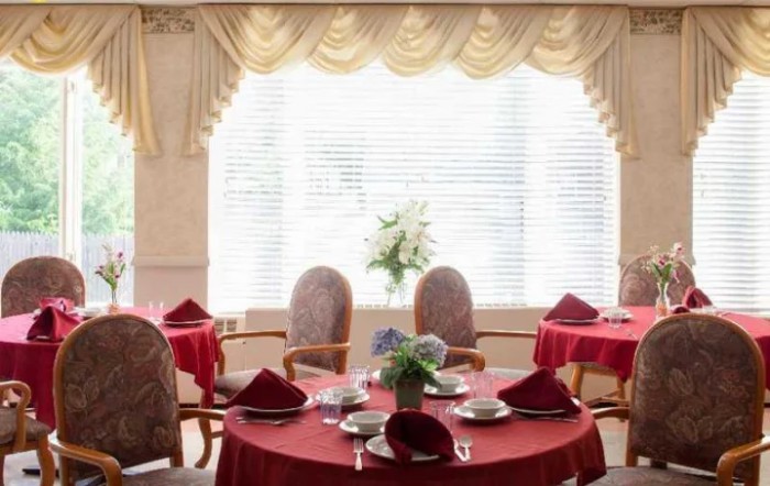 A formal dining area with red tablecloths, neatly arranged settings, and elegant curtains.