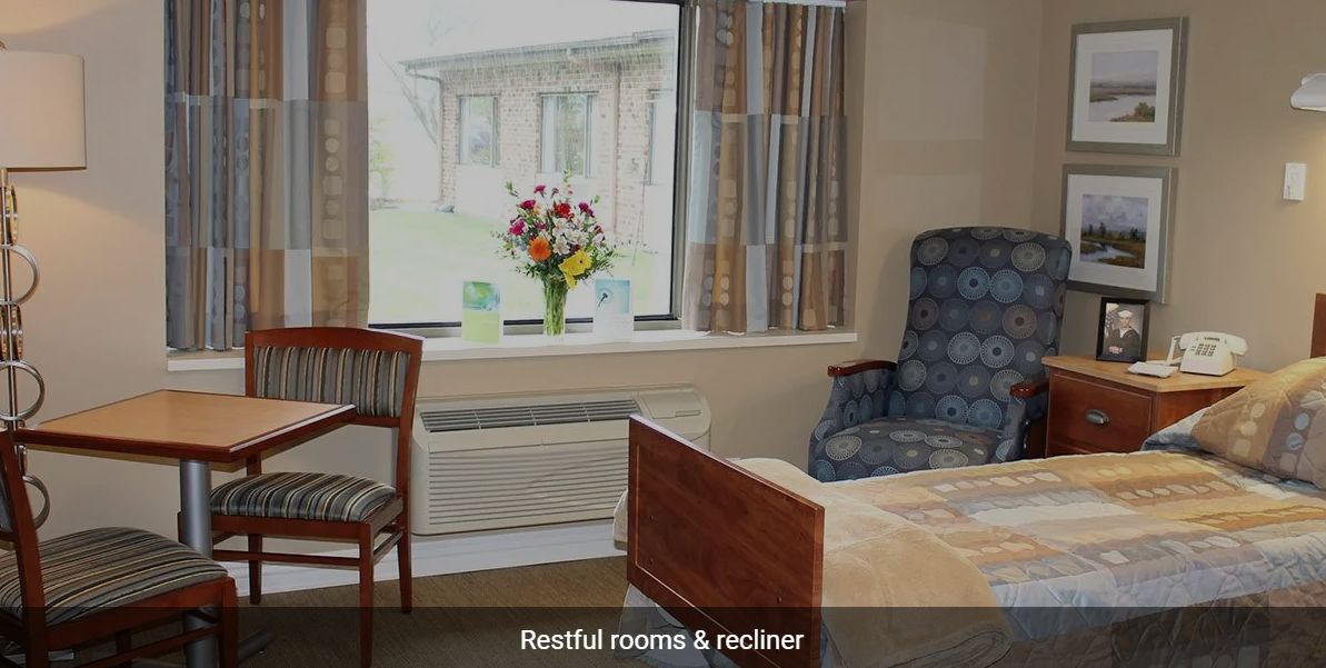 A restful room featuring a bed, recliner, and window with curtains.