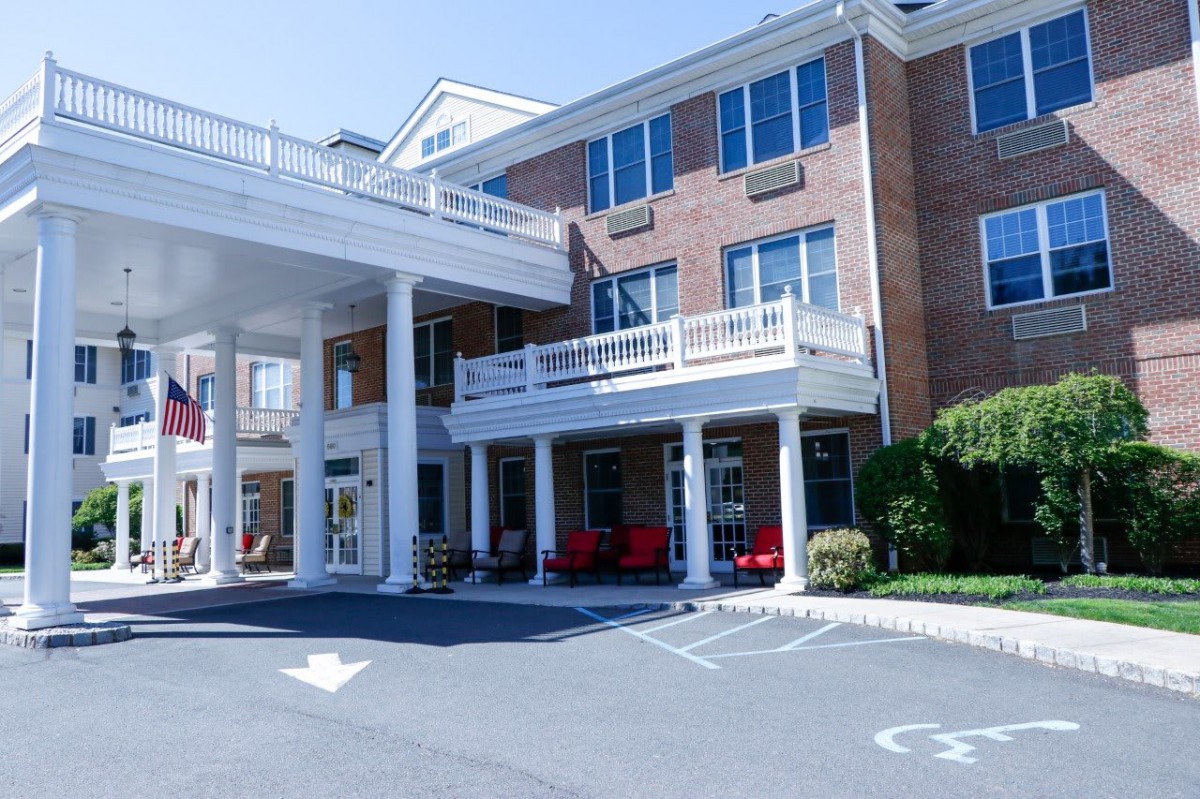 A large building with a columned entrance and multiple windows, featuring a parking area in front.