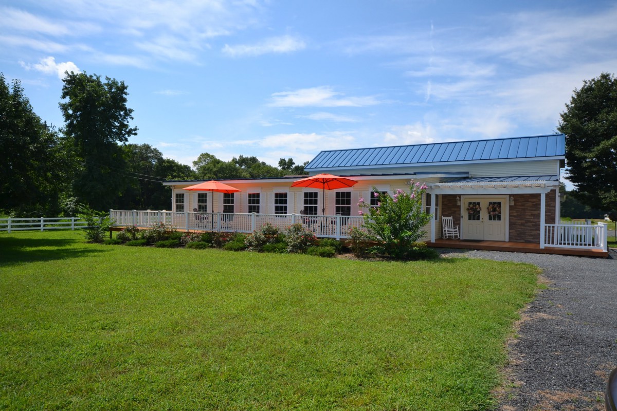 A small building with a blue roof and outdoor patio umbrellas, surrounded by green grass under a clear blue sky.