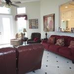 A cozy living room with leather sofas, decorative pillows, and wall art, featuring large windows that let in natural light.