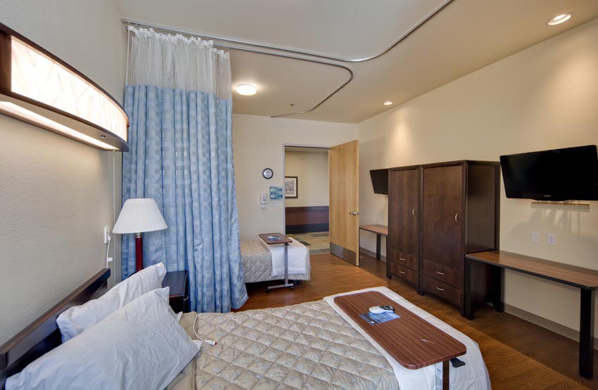 A hospital room with a patient bed, curtain, and TV.