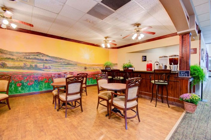 A cozy restaurant interior featuring a colorful mural, wooden tables and chairs, and a bar area.