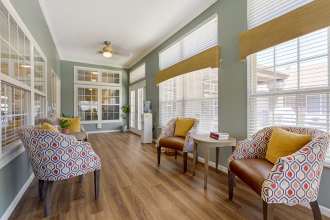 A cozy seating area with wooden flooring, featuring four chairs and large windows letting in natural light.