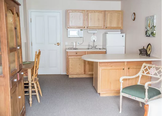 A small kitchen area with wooden cabinets, a refrigerator, and a dining table with chairs.