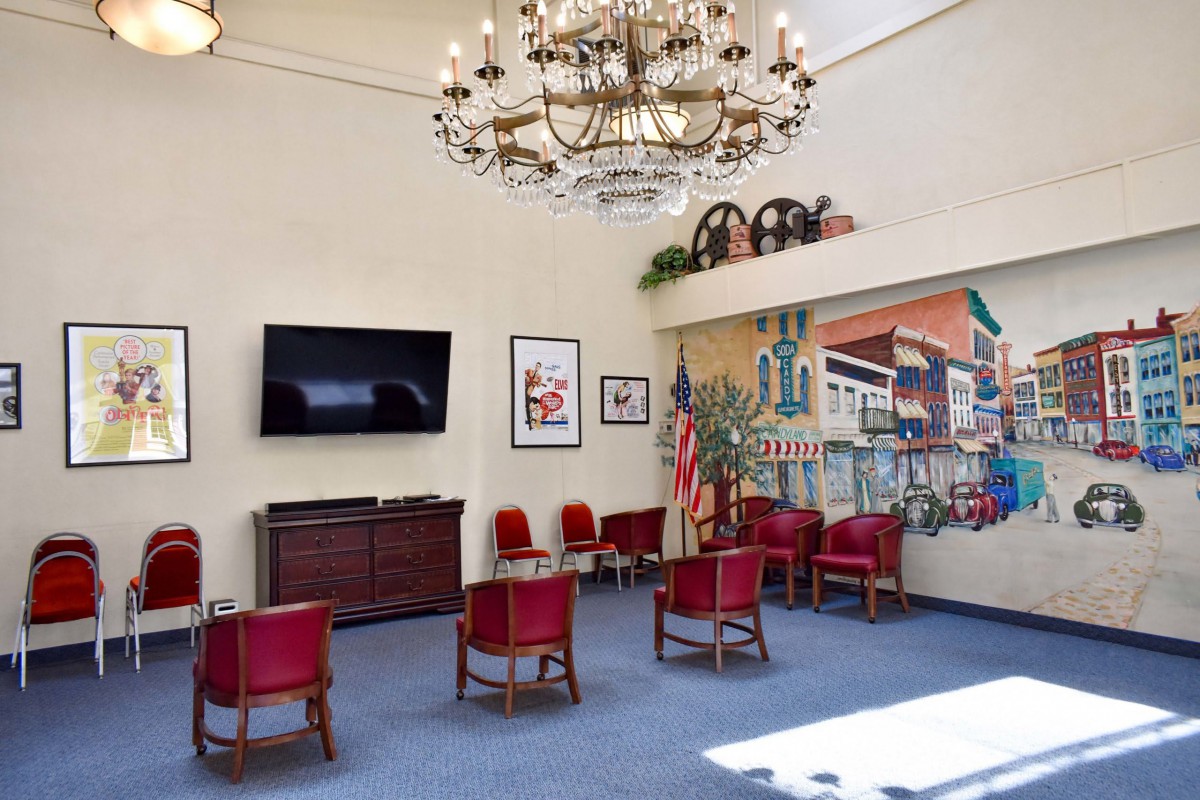 A cozy lobby area with red chairs, a chandelier, and wall decorations.