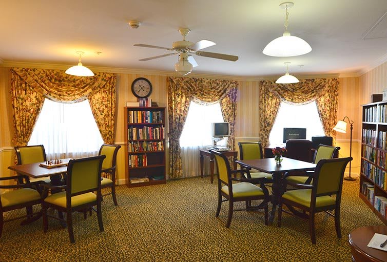 A cozy library reading area with tables, chairs, and a bookshelf under warm lighting.