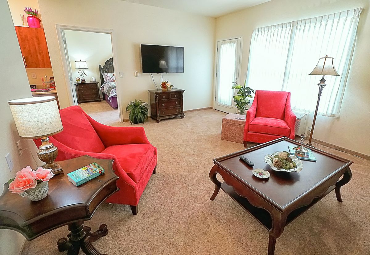 A cozy living room with red chairs, a flatscreen TV, and abundant natural lighting.