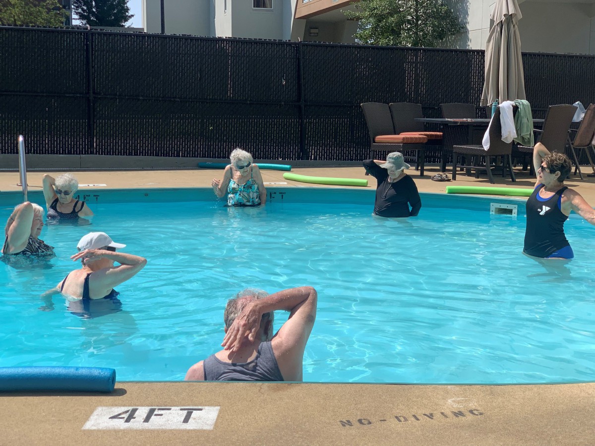A group of people participating in a water aerobics class in an outdoor swimming pool.