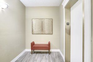 A minimalist hallway with a red bench and framed artwork on the wall.