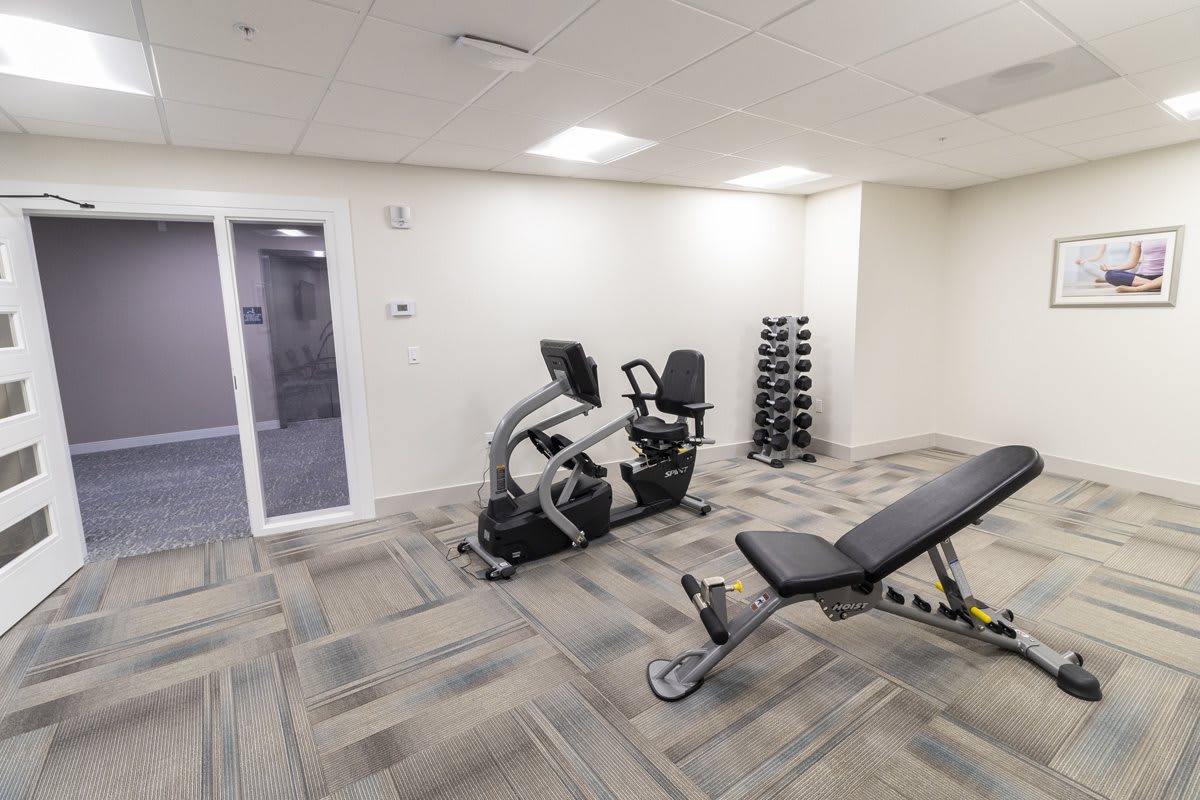 A small gym with an exercise bike, adjustable bench, and dumbbell rack.