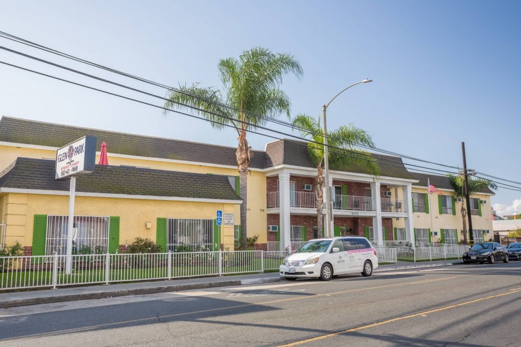 A street view of a hotel with palm trees and a car parked in front.