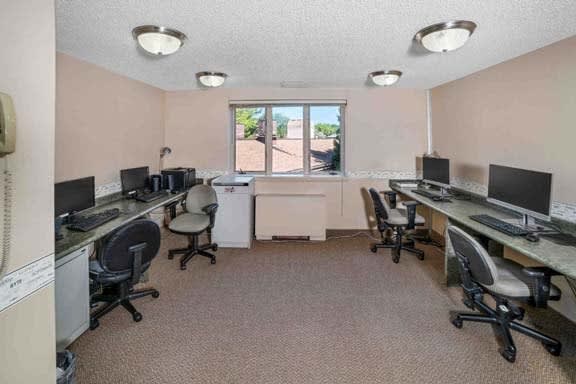 A small office space equipped with computers, desks, and chairs, illuminated by ceiling lights.