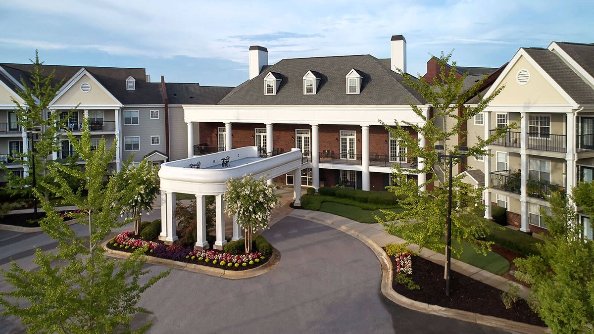 A colonial-style building with a circular driveway and landscaped garden.