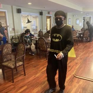 A person in a Batman costume walks through an indoor social gathering.