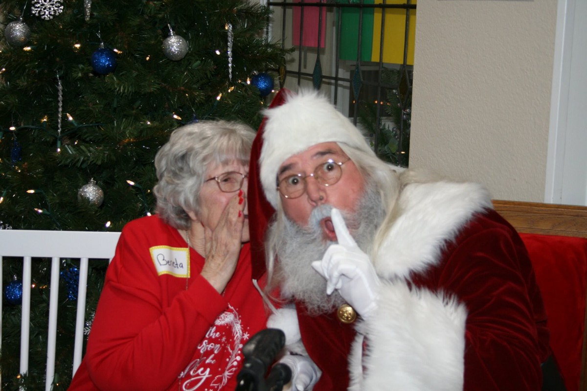 An elderly woman whispers to Santa Claus in a festive setting.