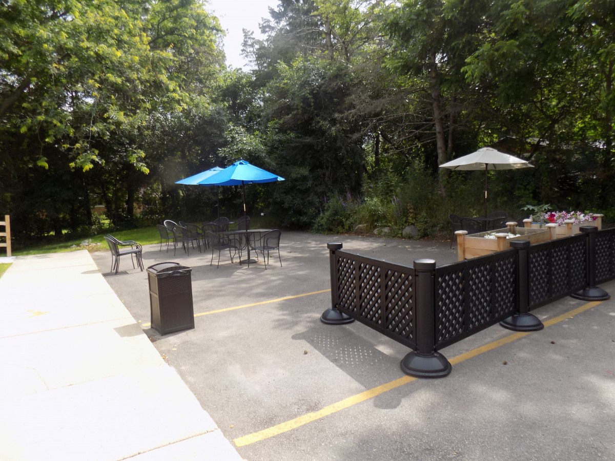 A quiet outdoor patio area with tables, chairs, and umbrellas surrounded by trees.