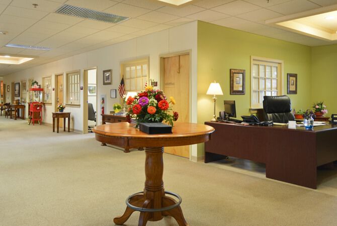 A welcoming office reception area featuring a round table with a flower arrangement, desks, and ambient lighting.