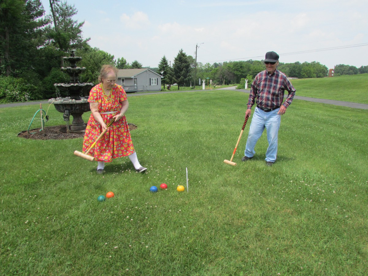 A couple playing croquet on a sunny day in a grassy field.