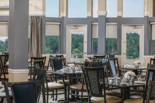 A well-lit dining area with elegant tables and chairs, offering a view through large windows.