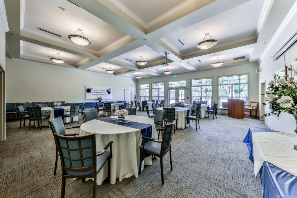 Spacious conference room set up with tables and chairs, illuminated by ceiling lights and natural light from large windows.